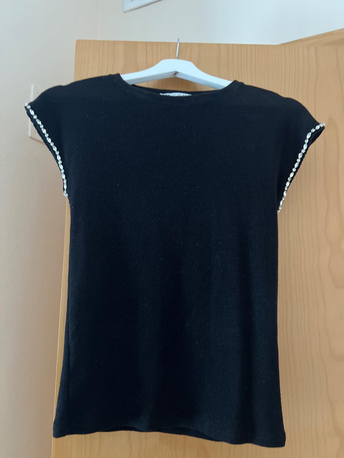 Front view of a black t-shirt with embellishments on the sleeves.