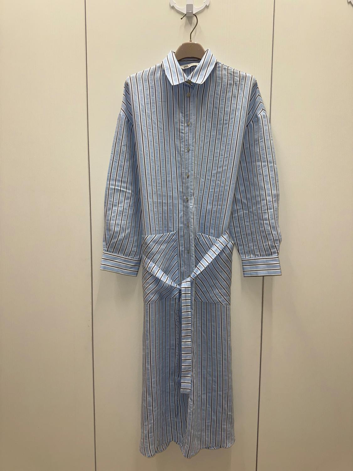 Blue and white striped shirt dress hanging on a hanger against a beige background. Long sleeves and matching belt.
