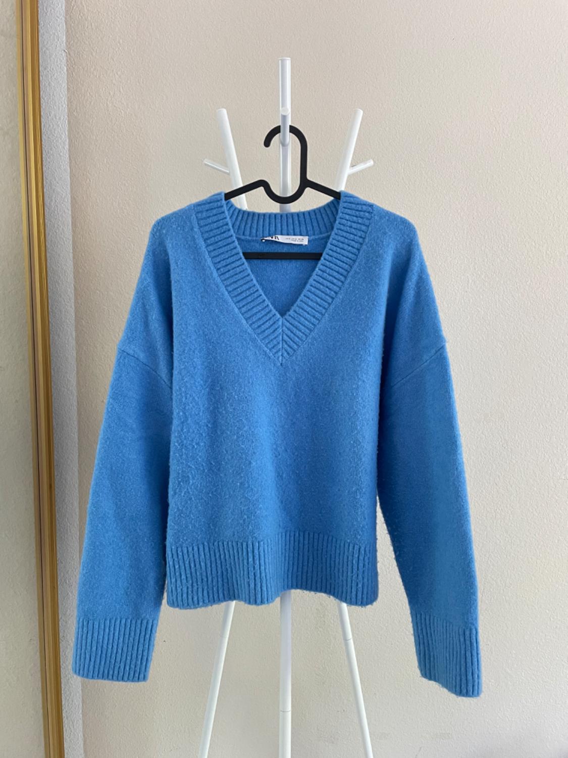 Blue V-neck sweater hanging on a white clothes rack against a beige background.