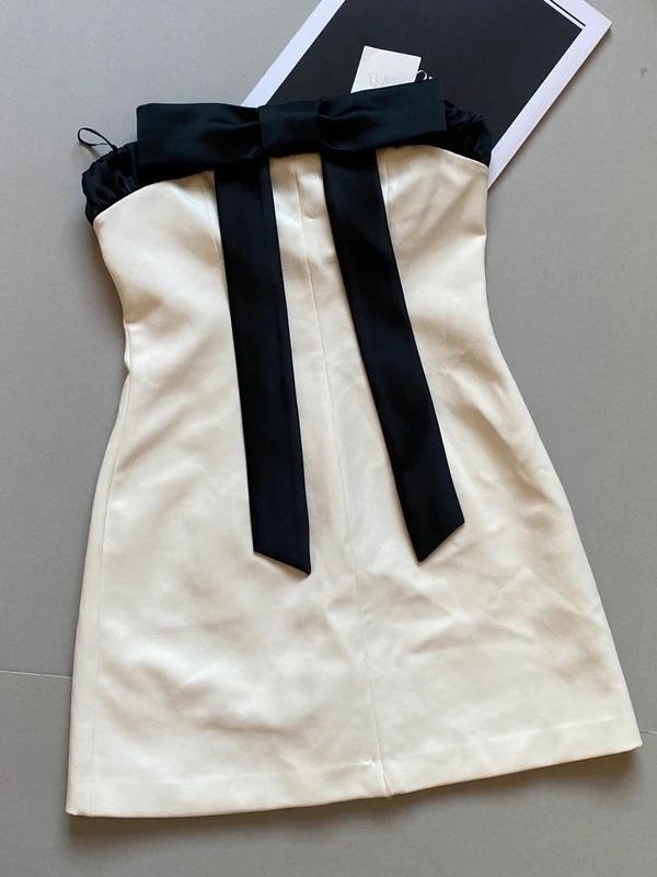 Cream strapless dress with black bow on the neckline, on a grey background with black and white papers.