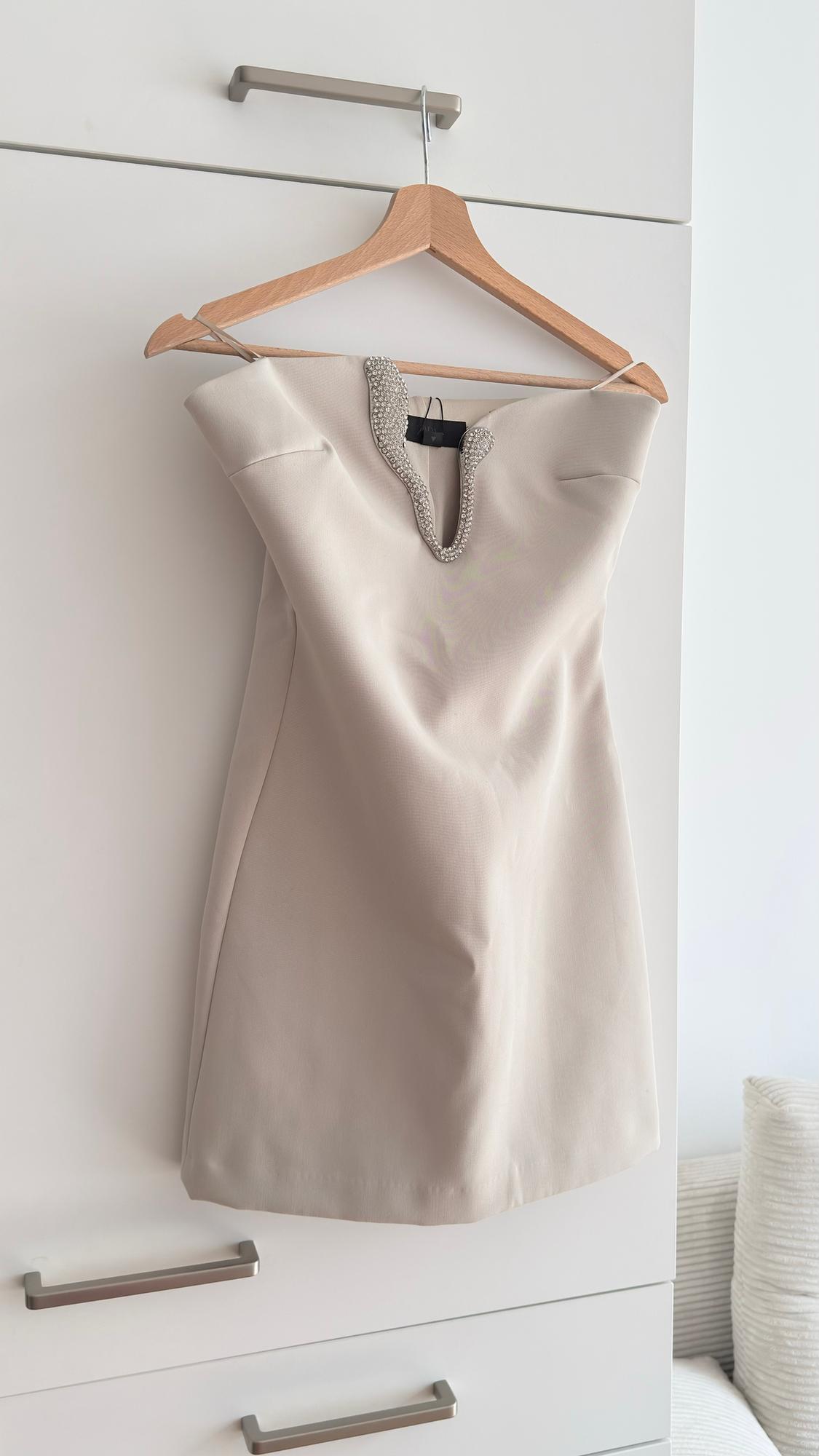 Beige sleeveless dress with a decorated neckline, hanging on a wooden hanger over a white wardrobe.