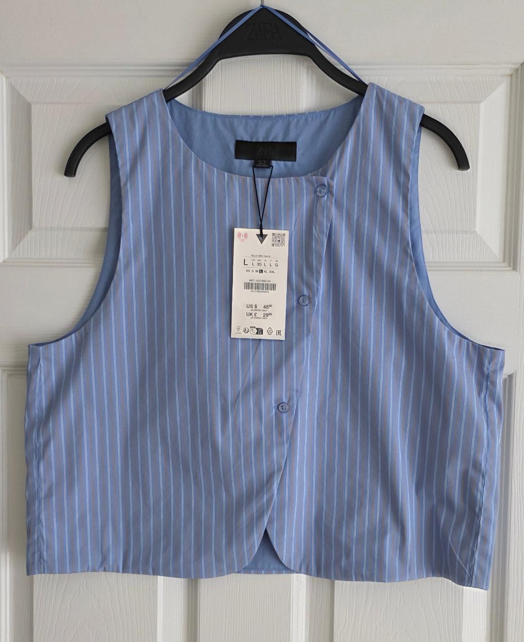 Blue vest with white vertical stripes, hanging on a black Zara hanger in front of a white door, visible tag with price and size.