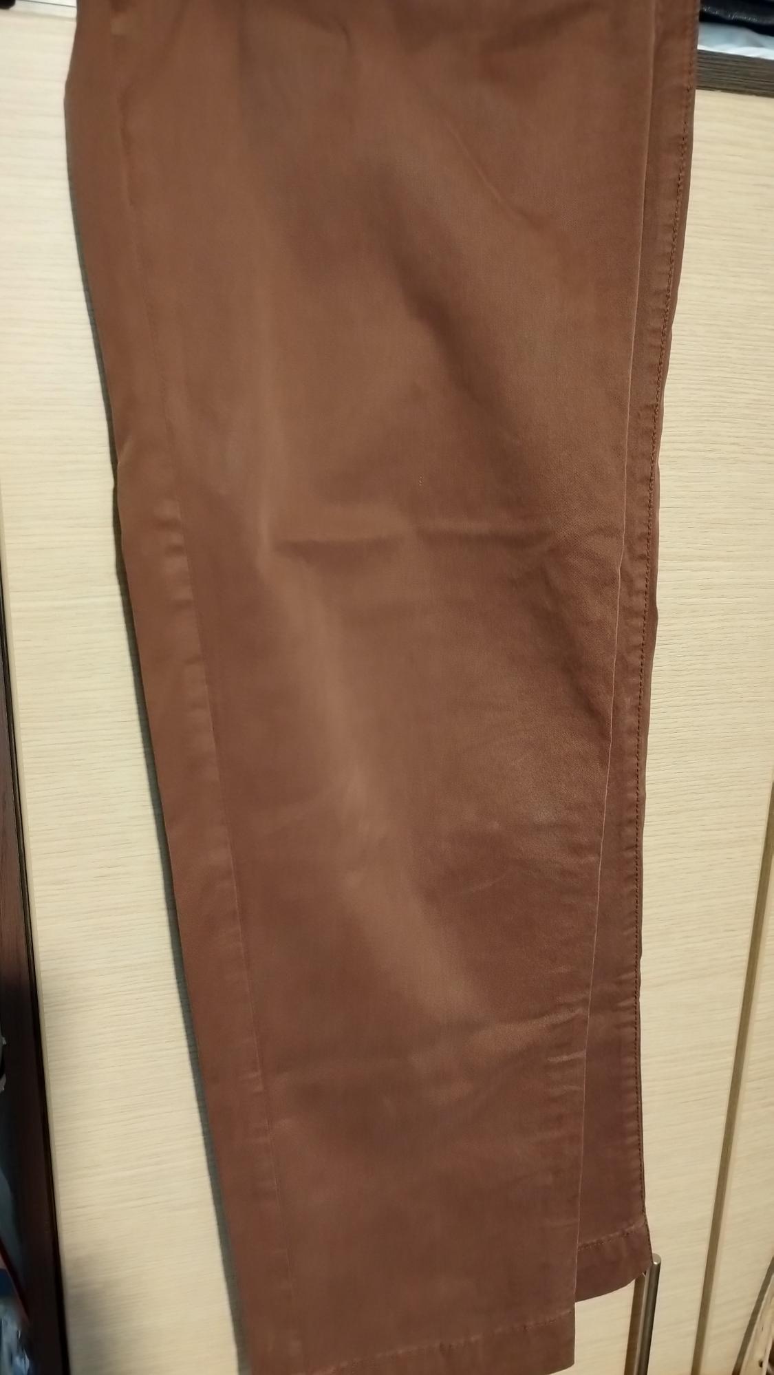 Brown trousers hanging over a light wooden door, showing stitching details and fabric texture.