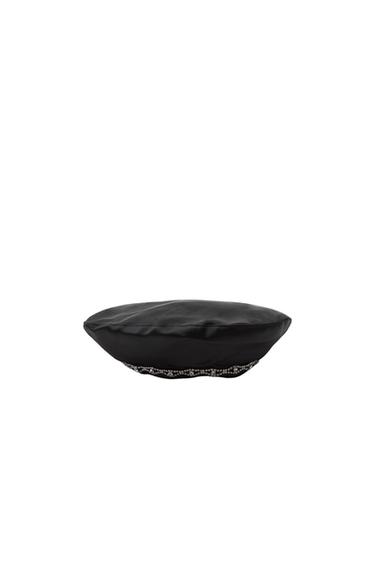 Side view of a black beret with a decorative silver bead trim.