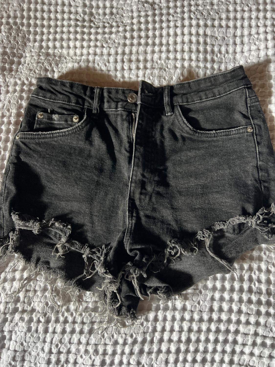 Black denim shorts with a frayed hem on a textured white fabric. Casual and relaxed style.