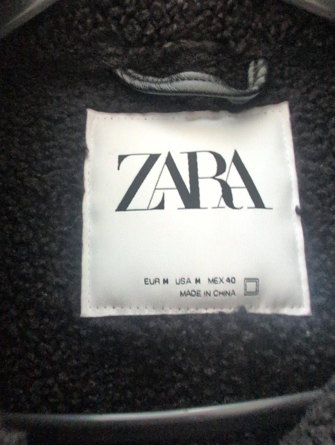Detail of a white label stitched onto dark textured fabric. Text: ZARA, EUR M USA M MEX 40, MADE IN CHINA.