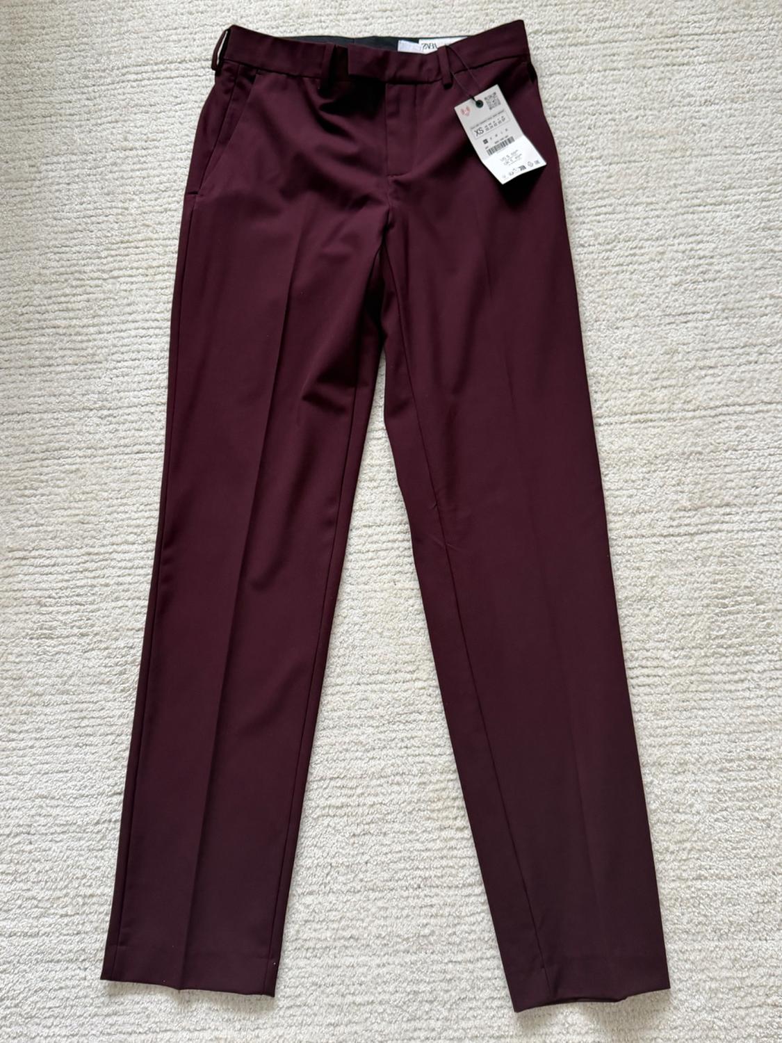 Burgundy dress pants with tags, placed on a light-colored rug. Classic design with pockets and belt loops.