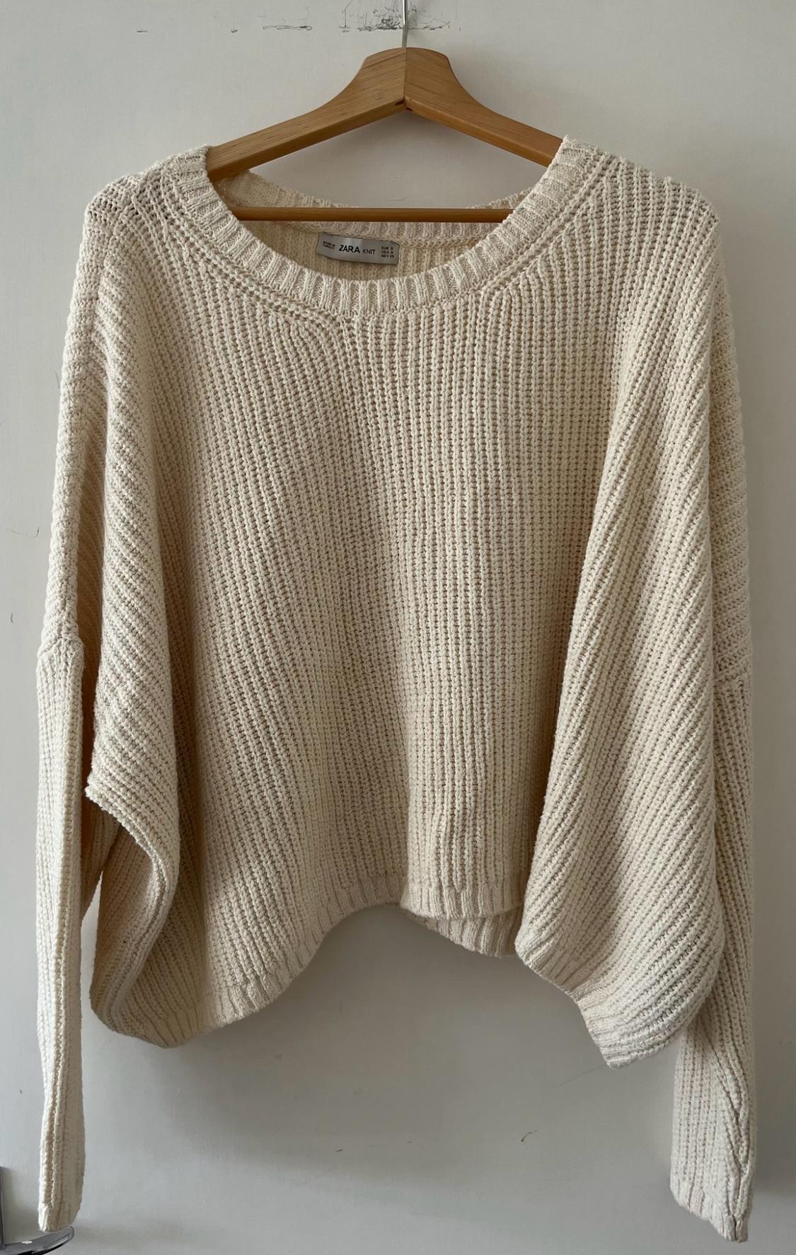 Cream-coloured loose-fit knit jumper hanging on a wooden hanger against a white background. Cosy style. Label with the text ZARA KNIT.