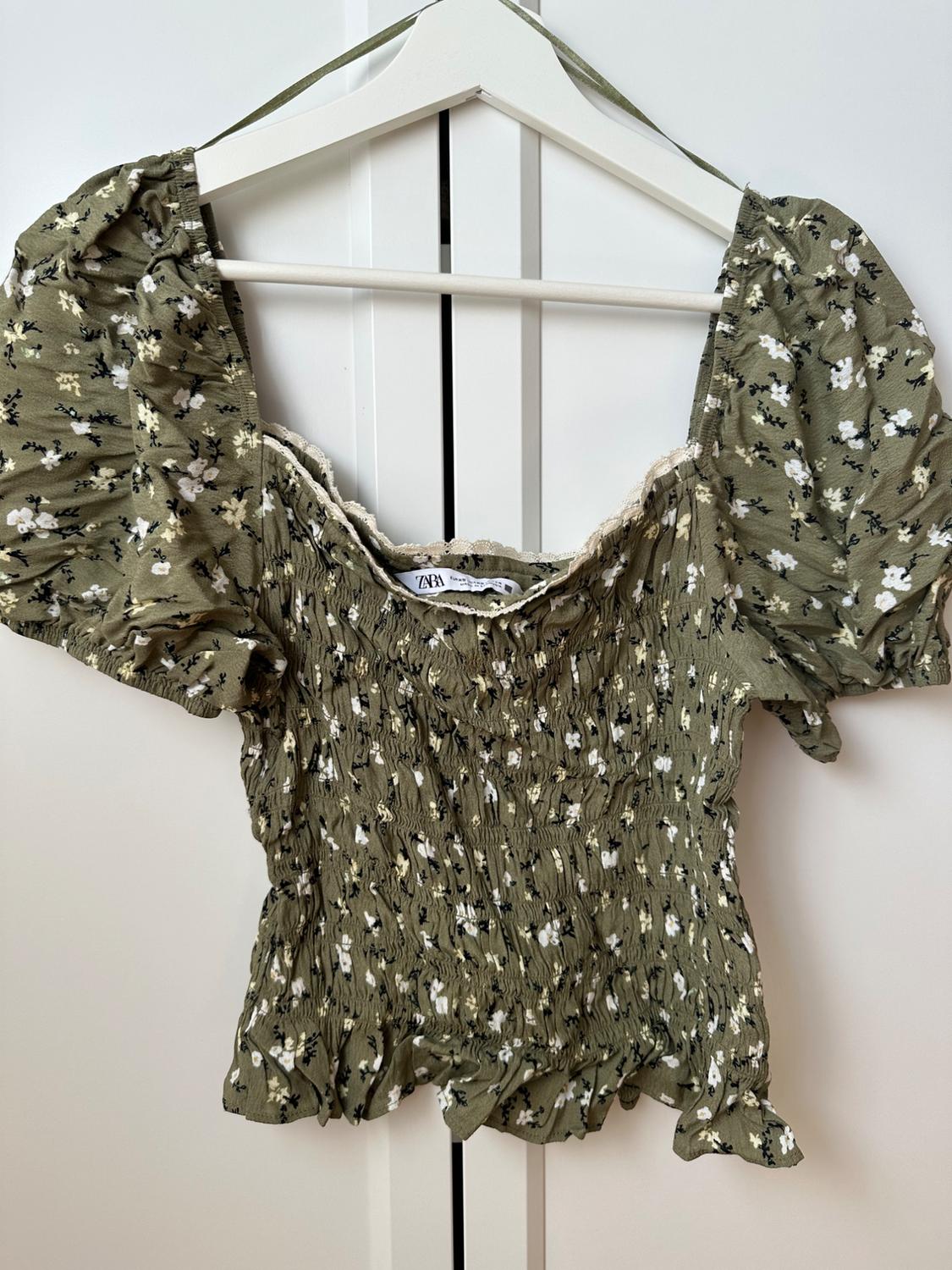 Green floral print top with a ruched body, puff sleeves, and lace trim on a white hanger. Label with the text ZARA.