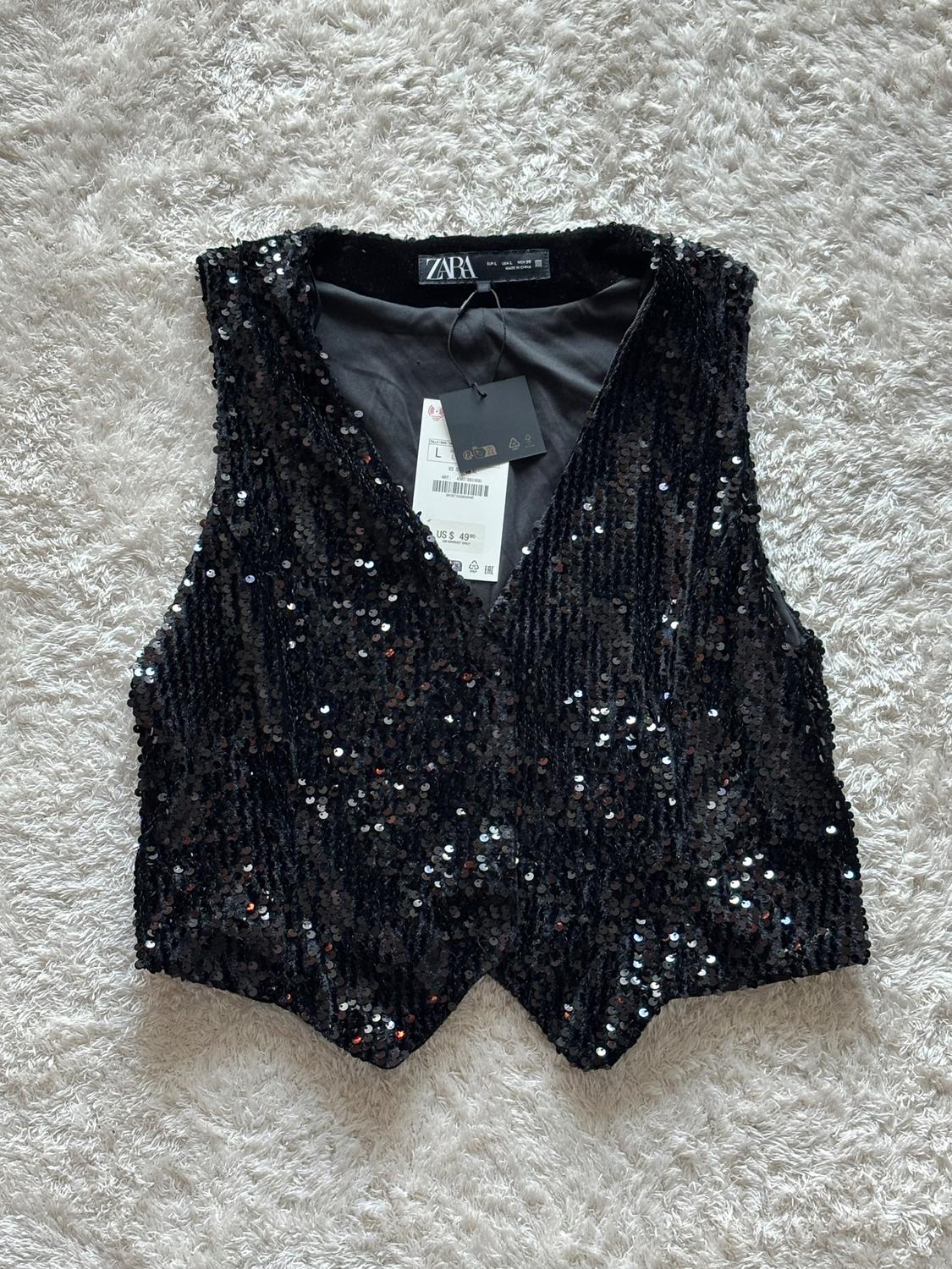 Black sequined waistcoat with Zara tag on white carpet. Tag shows size L and price US$ 49.90.