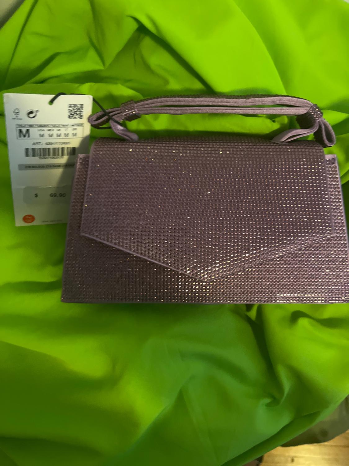 Bright purple handbag on green fabric. Visible tag with price of $69.90 and size M.