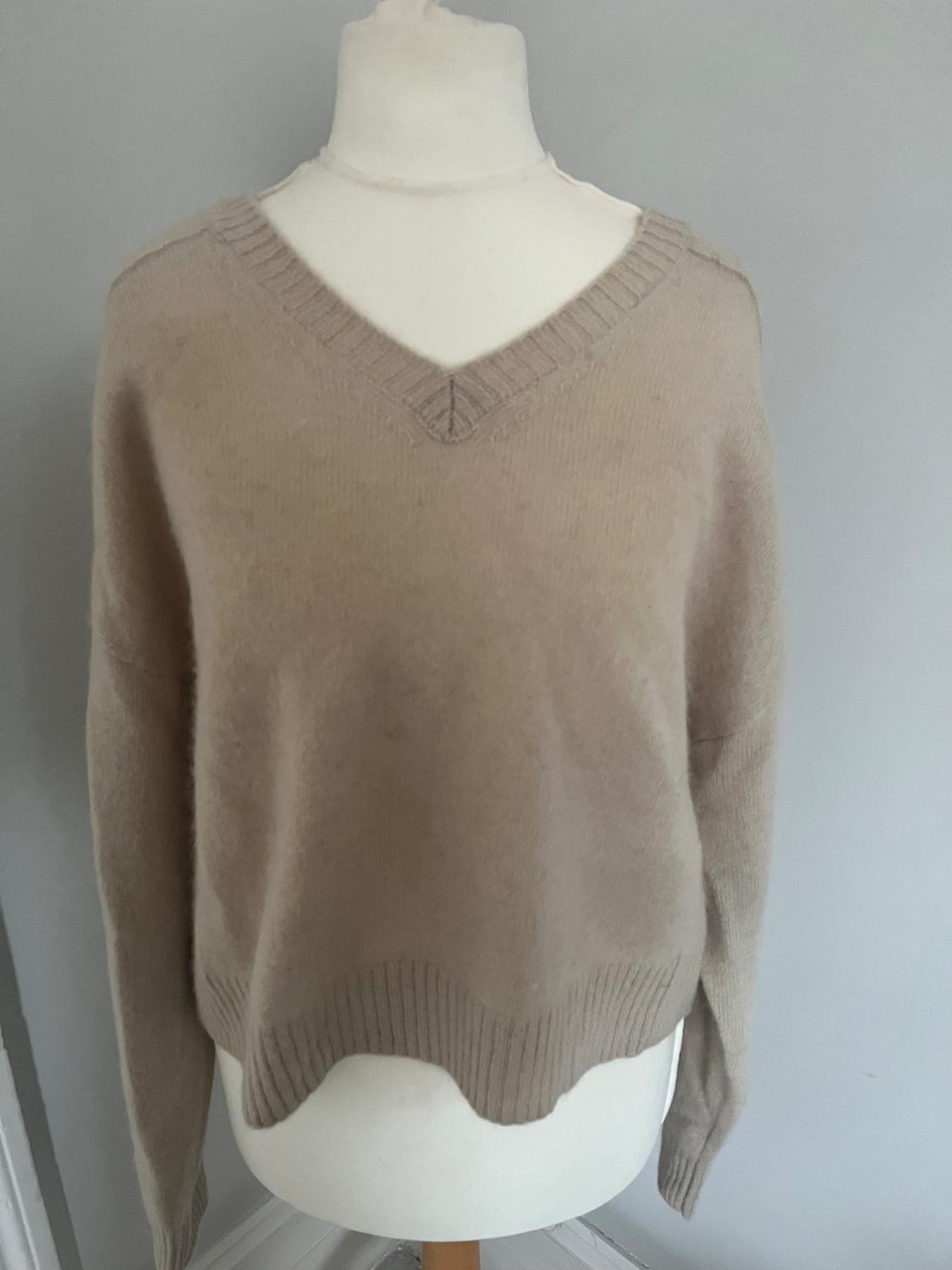 Beige knitted V-neck jumper on a white mannequin, light grey background.
