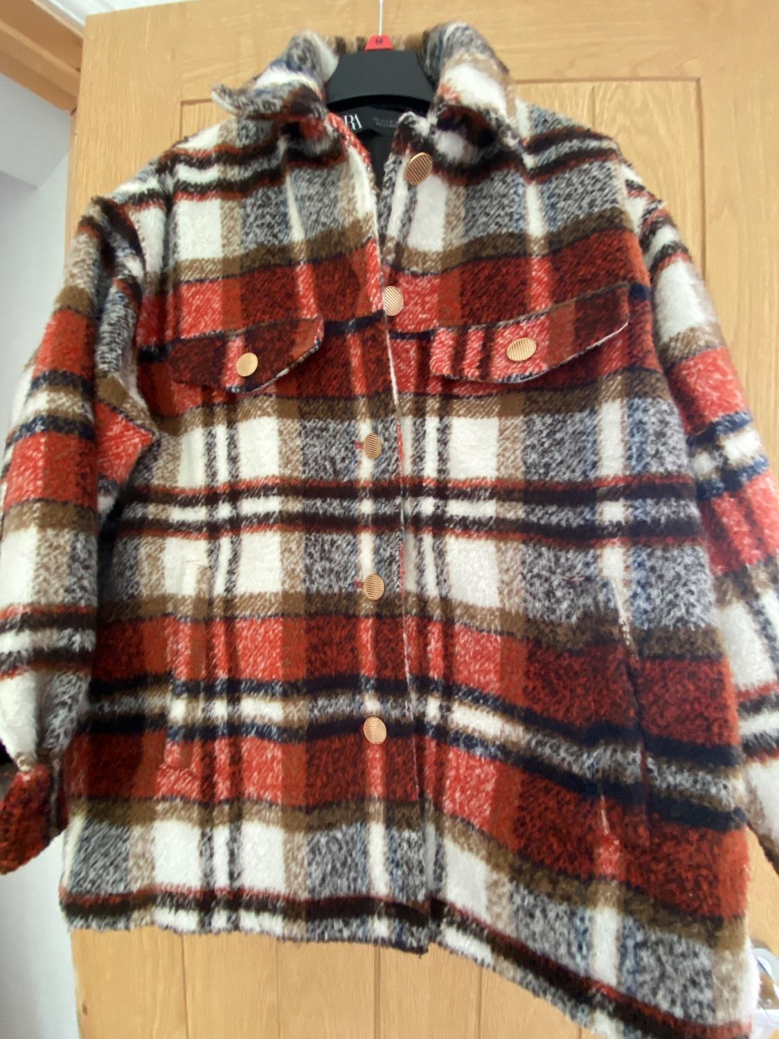 Checked jacket in shades of brown, red, and white, with gold buttons and front pockets, hanging on a wooden door.