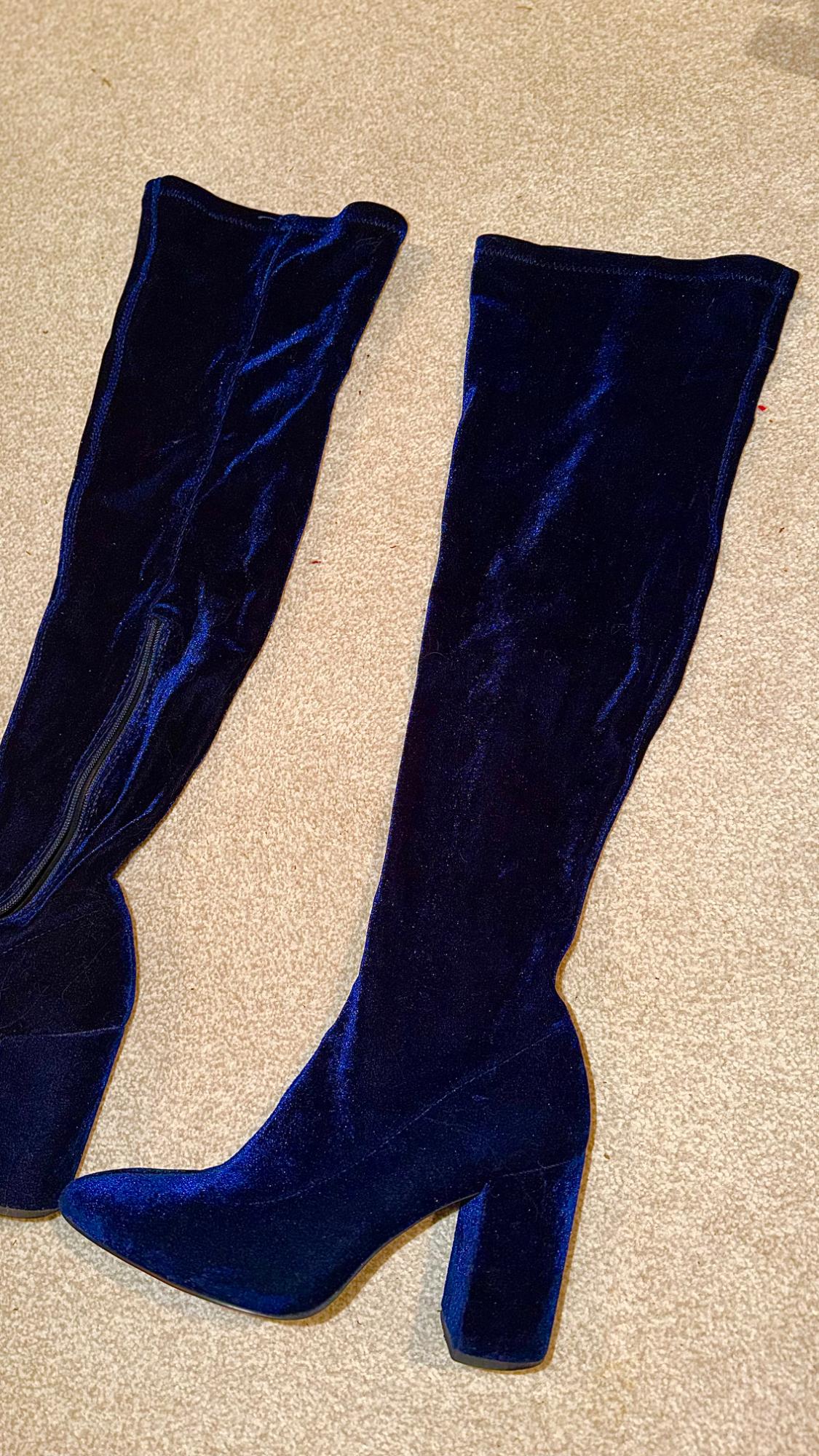 Dark blue velvet high-heeled boots with a chunky heel, on a beige carpet. One boot shows a side zip.