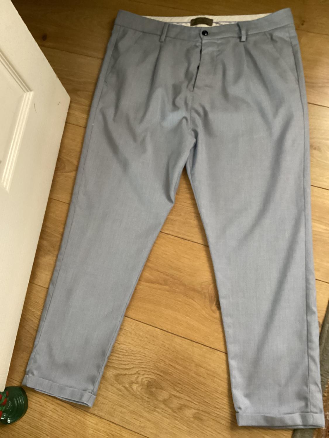 Front view of grey trousers with side pockets and button fastening.