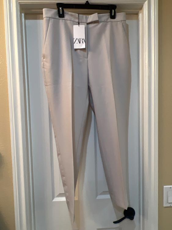 Beige pants hanging on a white door with a tag that says "ZARA". The door has a black handle.