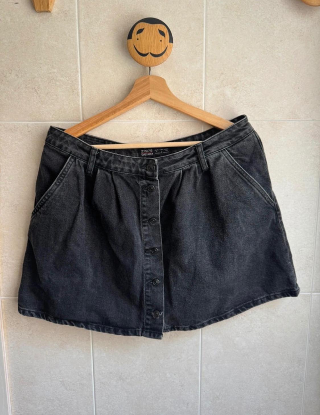 Black denim skirt hanging on a wooden hanger with a smiley face. Visible text: "Z1975 DENIM". Light tiled background.