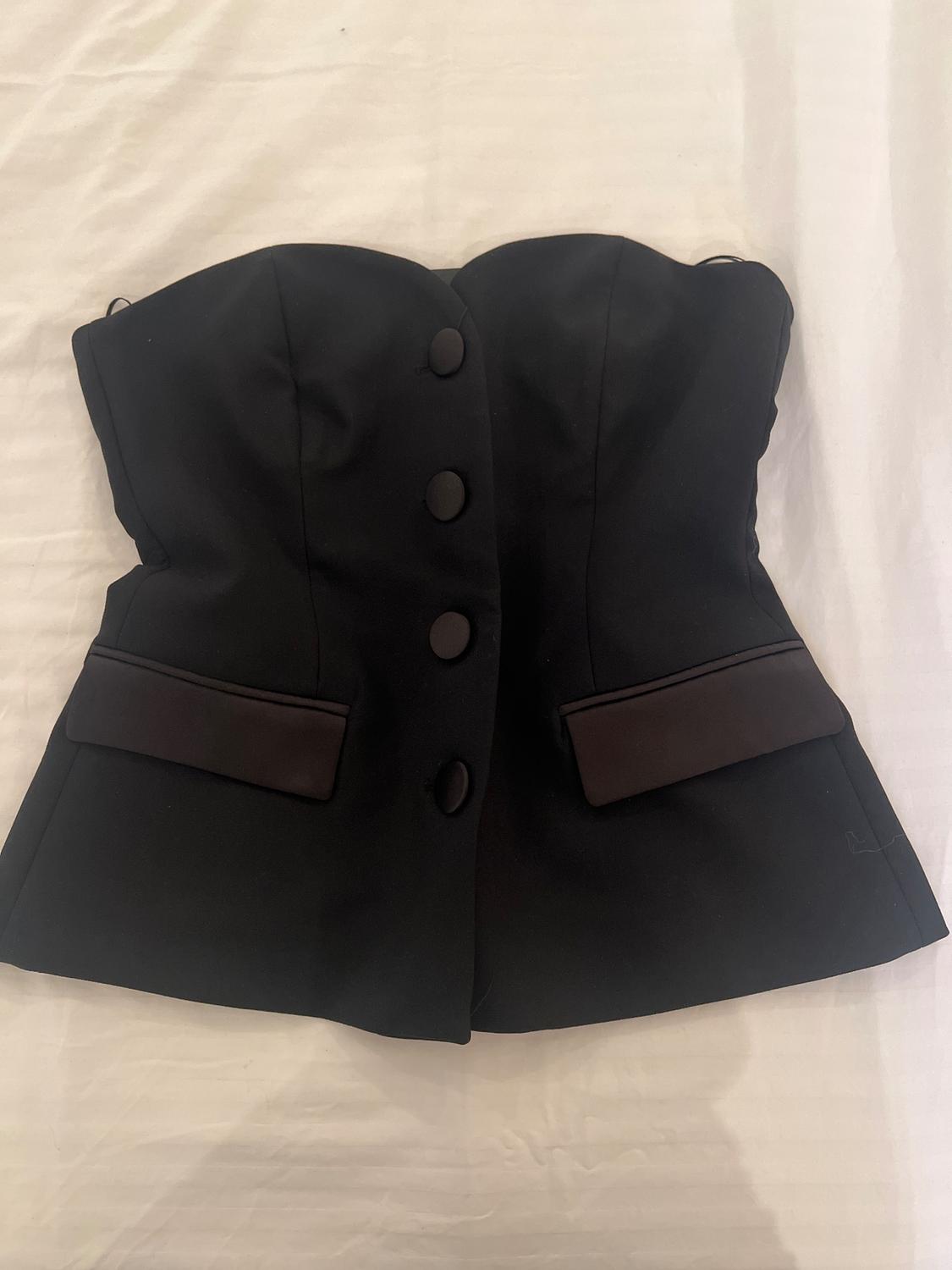 Black strapless corset with front buttons and decorative pockets, on a white background.