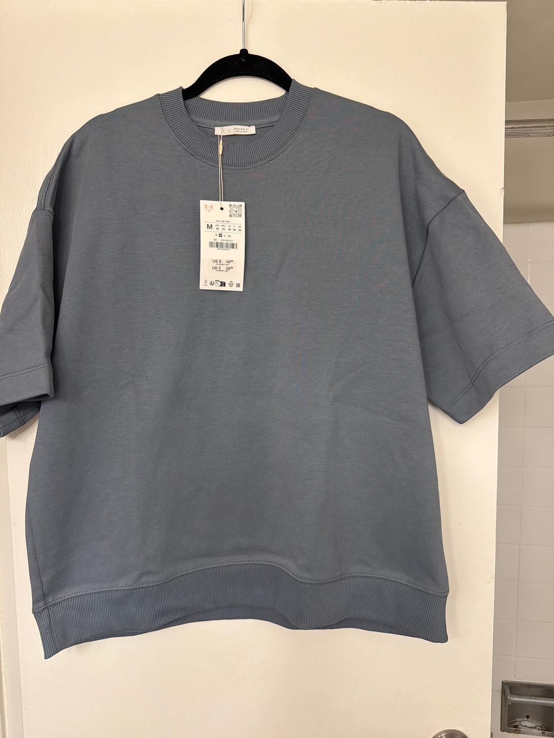 Blue short-sleeved t-shirt hanging on a black hanger, with price tag visible, over a white door.