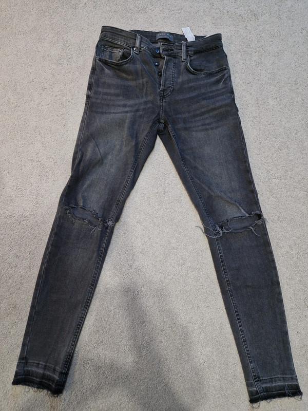 Front view of distressed black jeans with front pockets and rips at the knees.