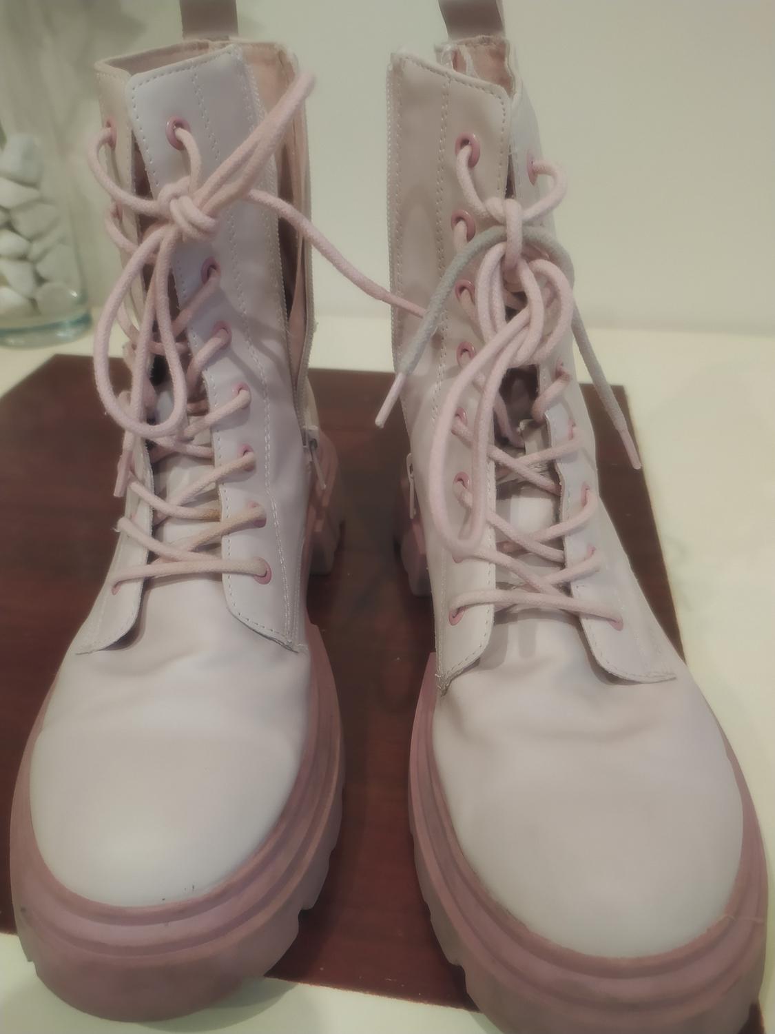 Pale pink leather boots with chunky laces on a wooden surface. Neutral background with decorative white stones.