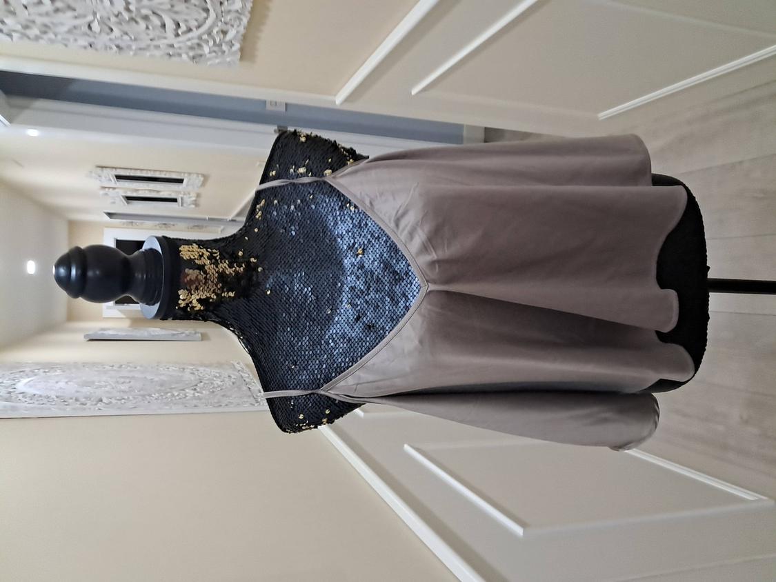Mannequin in a grey strappy dress, with a black and gold sequined top. Hallway background with light walls and decorations.