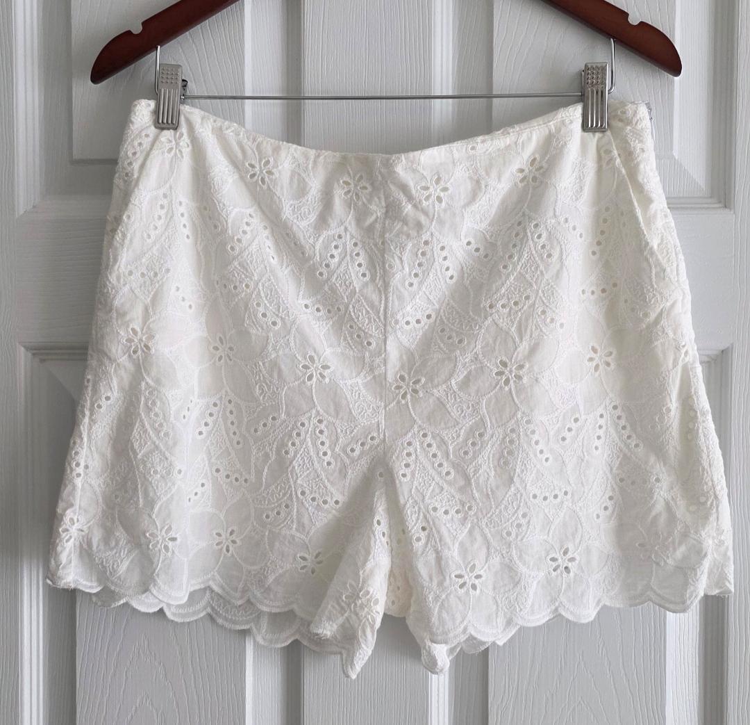 White lace shorts with a floral design hanging on a wooden hanger on a white door.