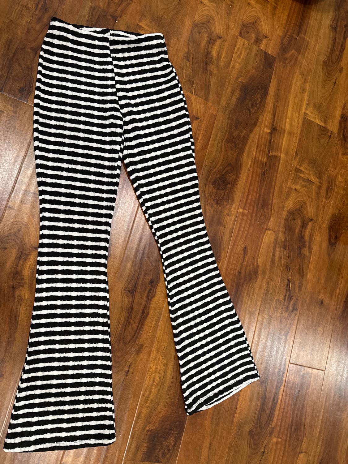 Flared trousers with black and white stripes on a brown wooden floor.