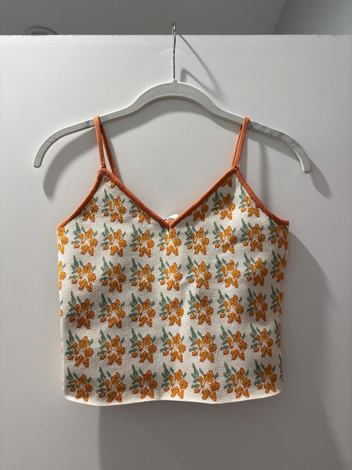 Orange and green floral print camisole on a white background, hanging on a white hanger against a white wall.