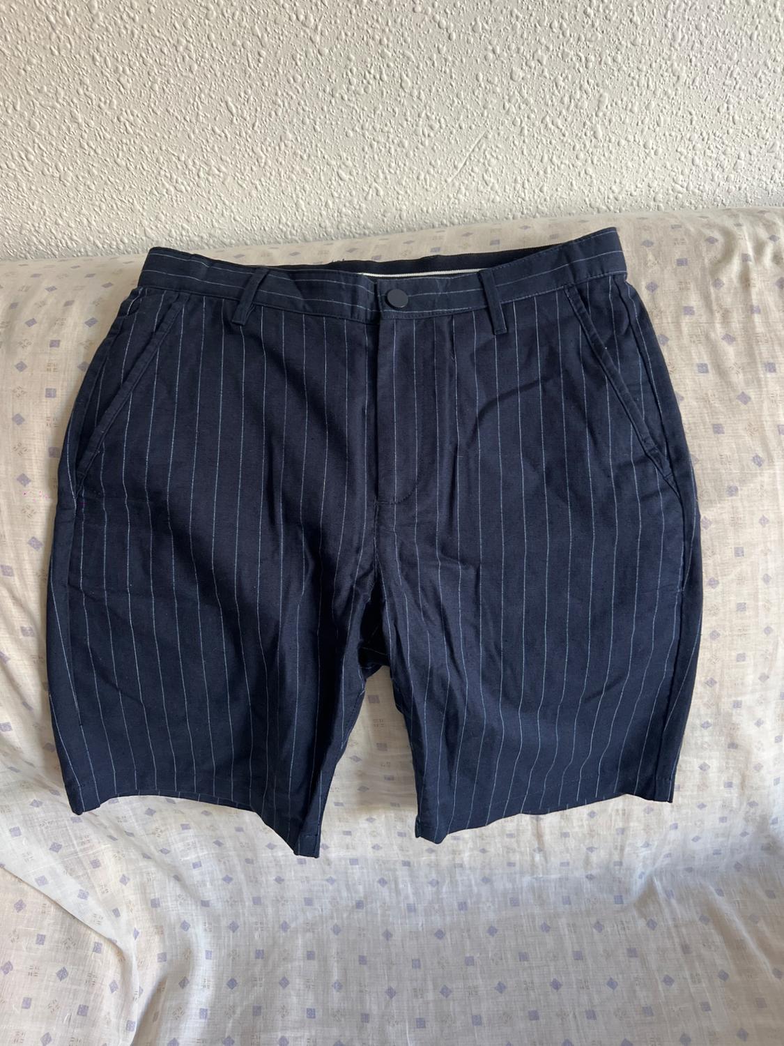 Navy shorts with white vertical stripes, placed on a light bedspread with a geometric pattern.