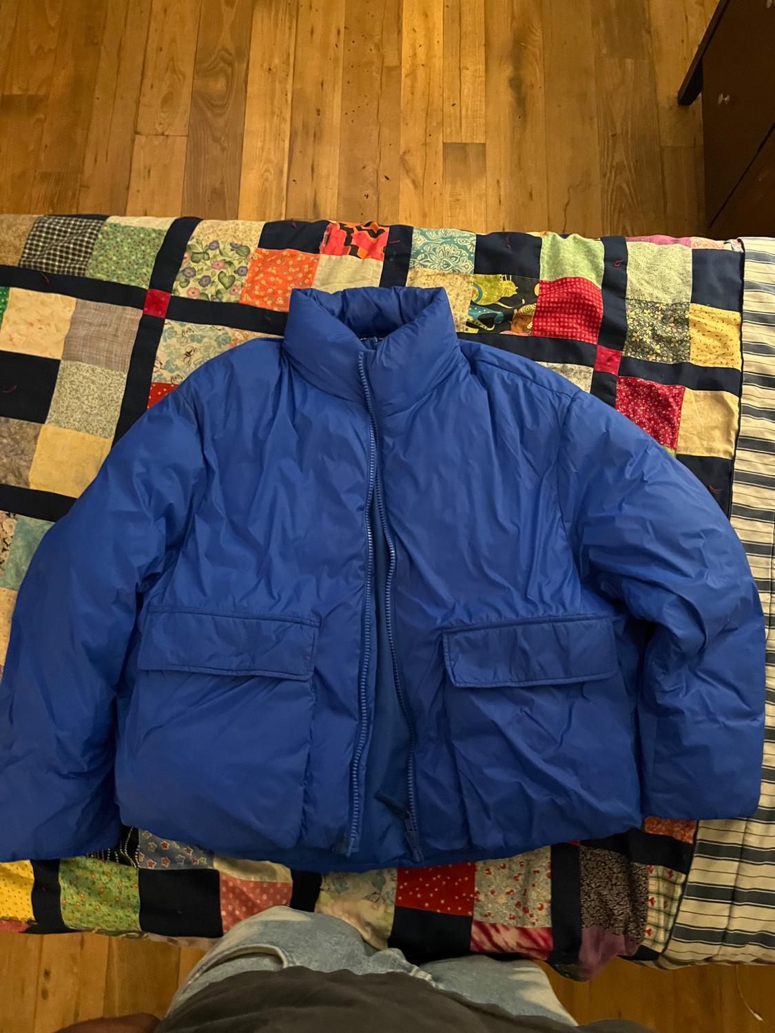 Quilted blue jacket on a colourful patchwork quilt on a wooden bed. Wooden floor visible in the background.