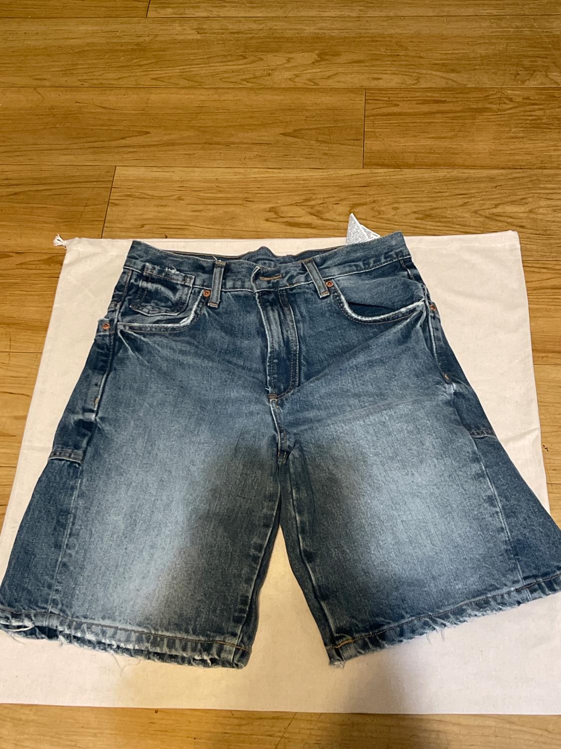 Distressed blue denim shorts with a frayed hem, on a light wood floor, over a white fabric.