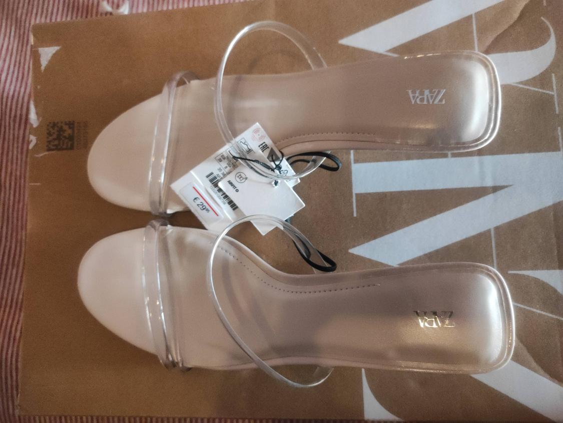 Beige sandals with clear straps and a price tag on a brown box with white lettering. Visible brand: ZARA.