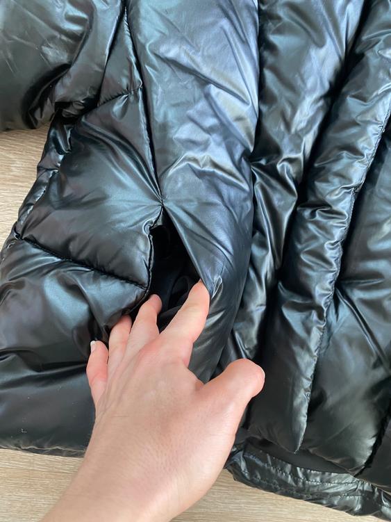 Hand touching a black puffer jacket on a light wood surface. The shiny texture of the material is visible.