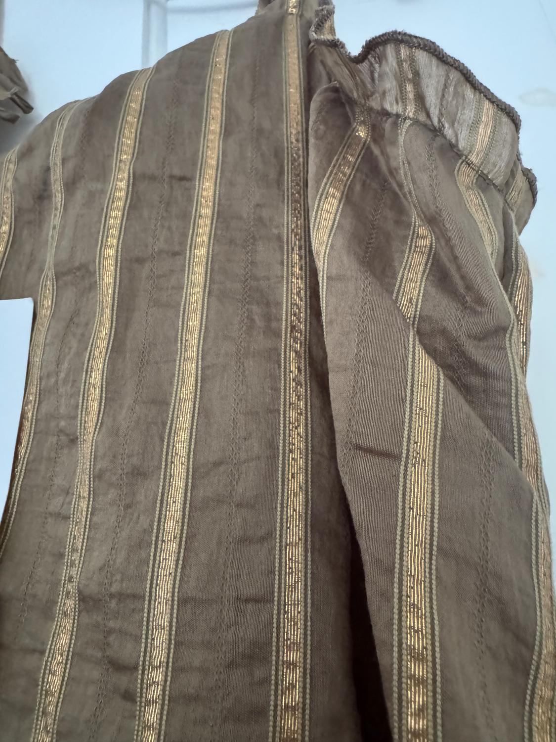 Close-up of a brown fabric with vertical gold stripes. The garment has a slightly wrinkled texture and is shown with folds.