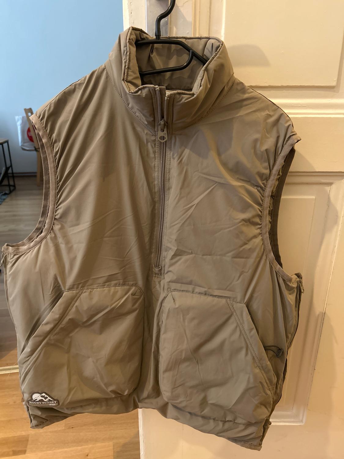 Beige gilet hanging on a hanger, with a front zip and two large pockets. "Rocky Mountain" logo on the bottom left.