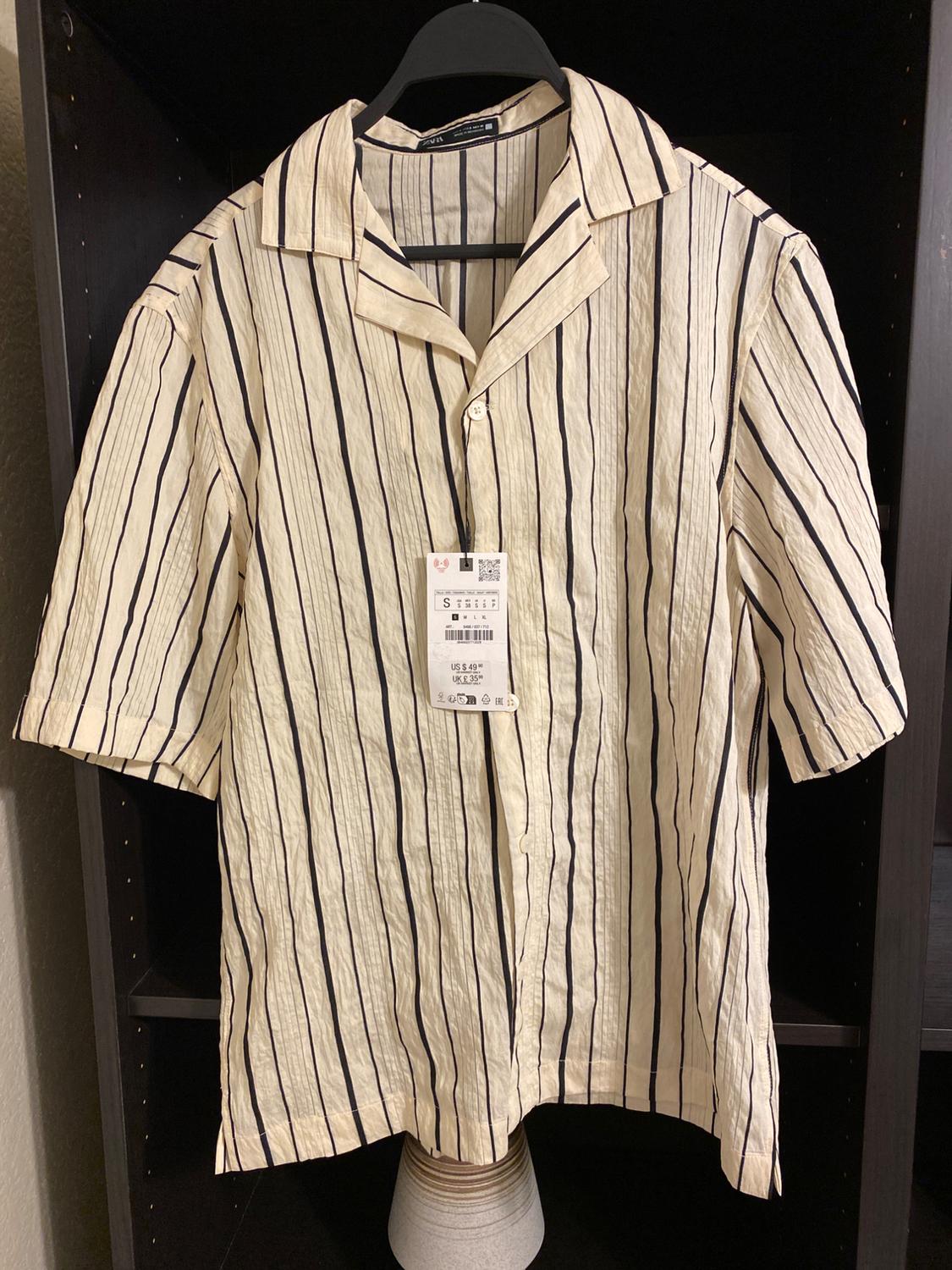 Black and beige vertical striped shirt hanging on a black hanger, with price tag visible in the centre.