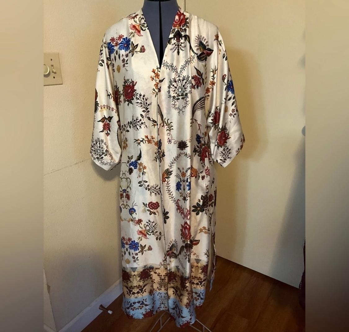 Long dress with a floral print in red, blue, and black tones on a white background, displayed on a mannequin in a room.