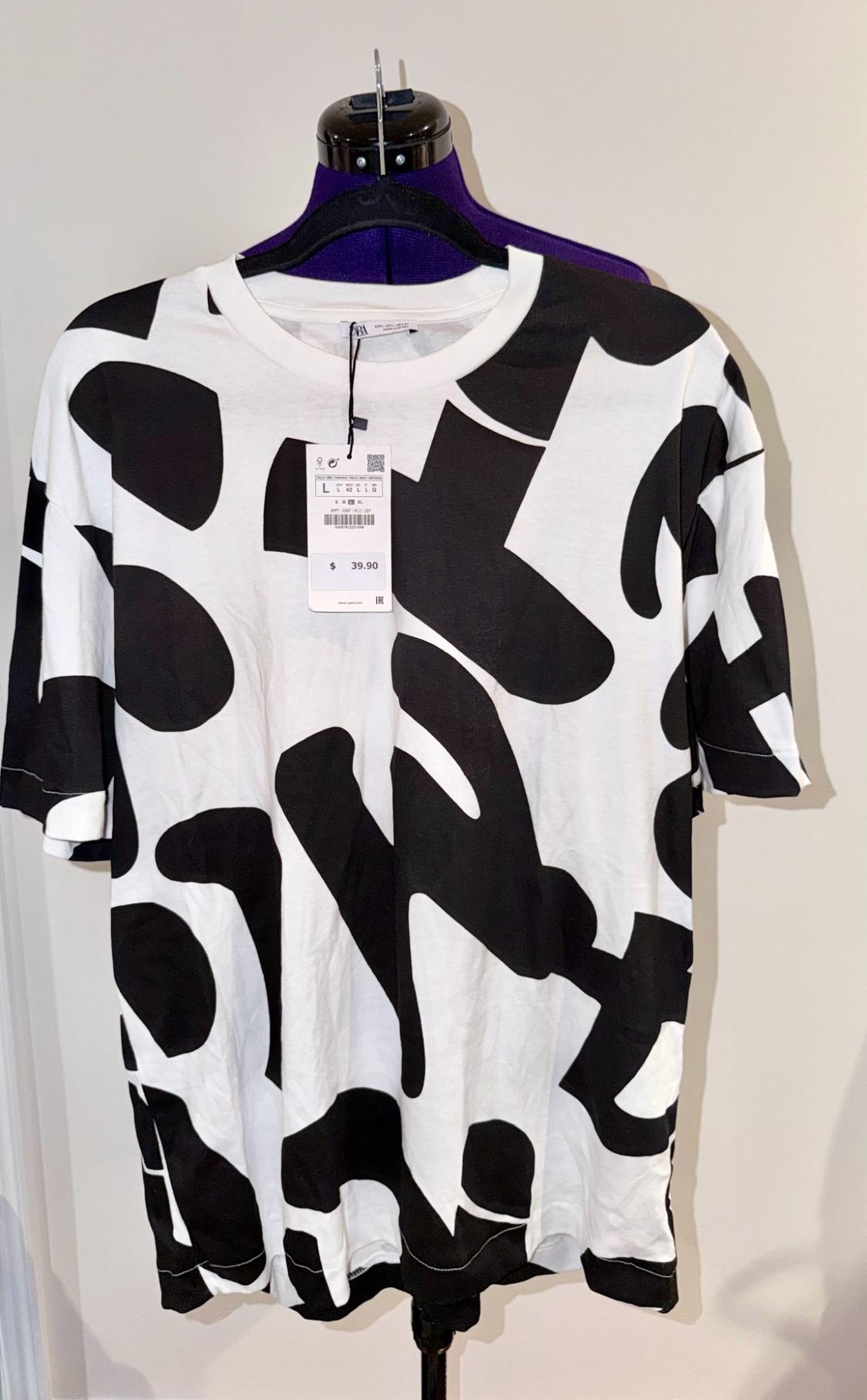 White short-sleeved T-shirt with a large black abstract print on a mannequin. Visible label with the text: ZARA, L, $39.90, EAC.