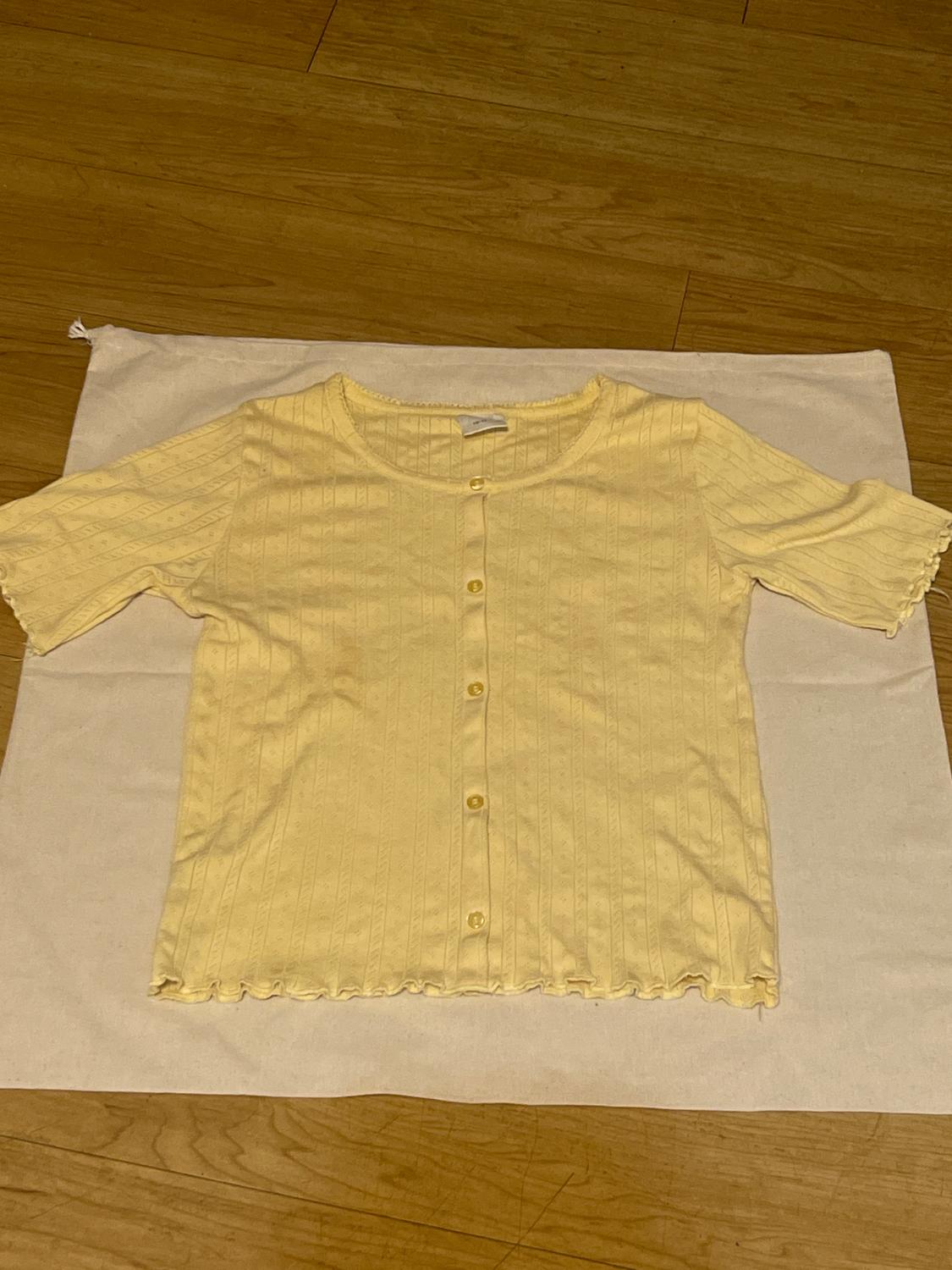 Yellow short-sleeved button-up shirt, placed on a white fabric on a wooden floor.