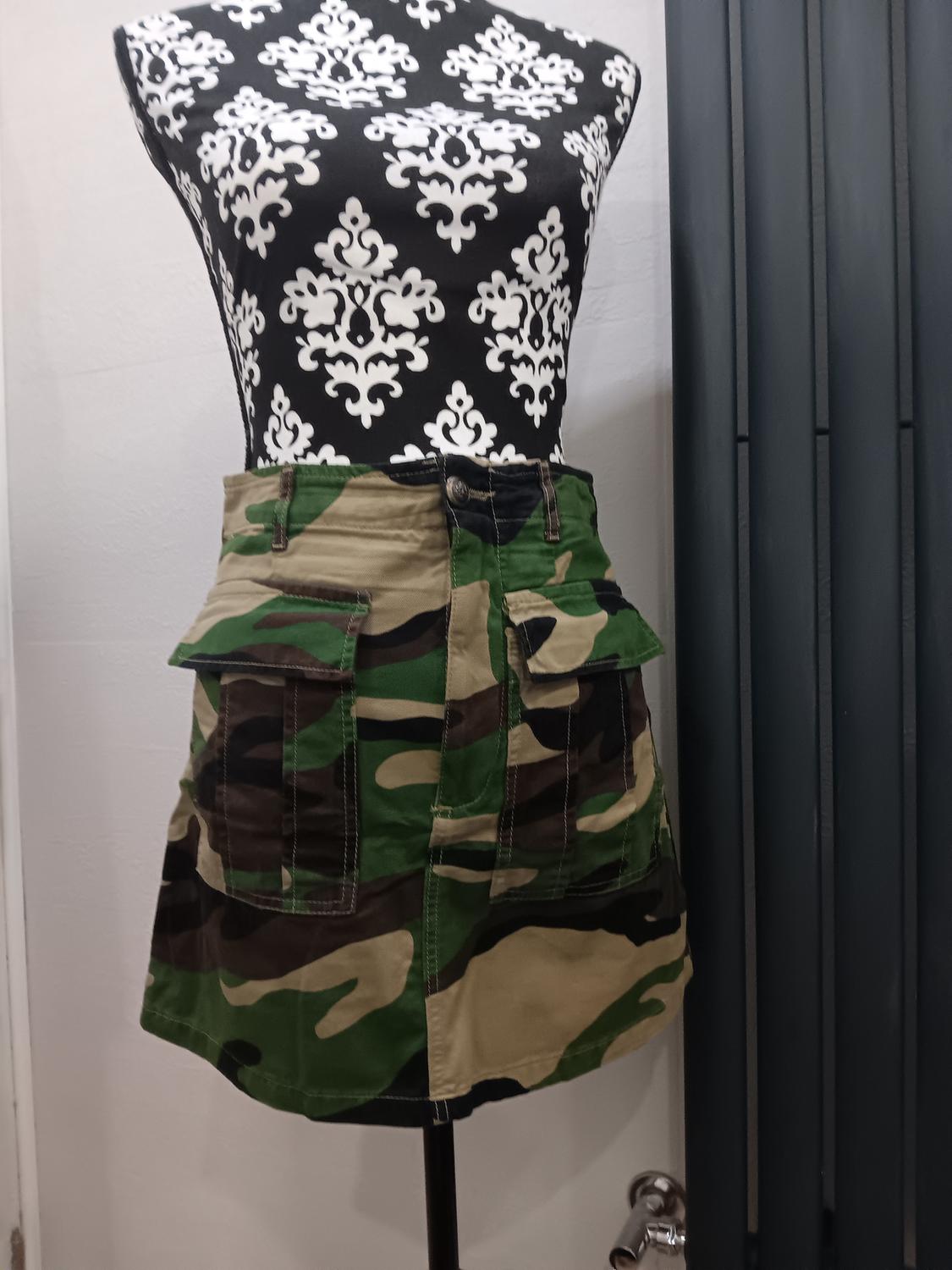 Mannequin in a black and white print blouse and a green and brown camouflage skirt, in an indoor setting.
