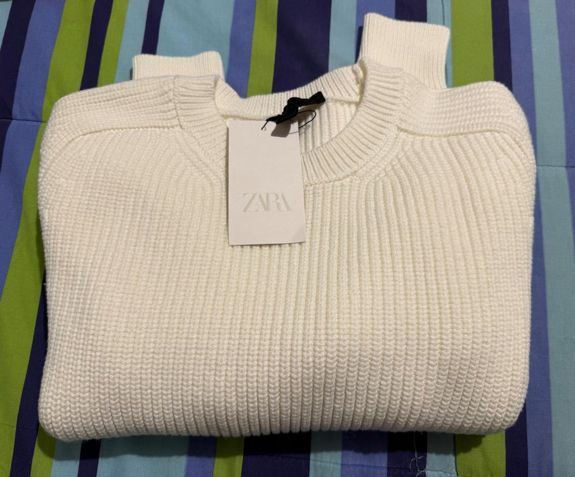 Chunky white knit jumper with Zara label, on a blue and green striped fabric.
