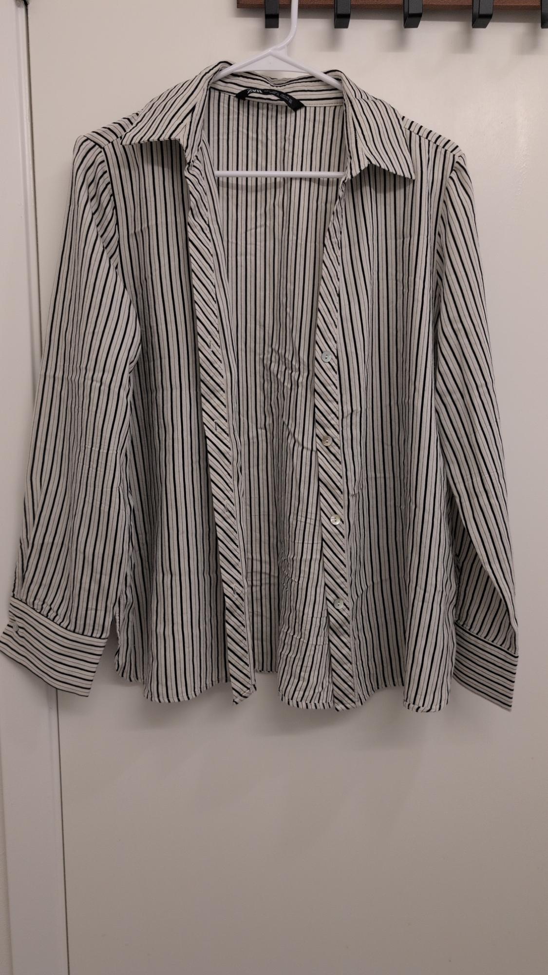 Black and white striped shirt hanging on a white hanger over a white door. Long sleeves and classic collar.