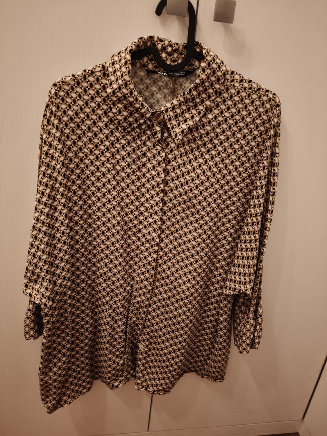 Black and white geometric print long-sleeved shirt, hanging on a black hanger over a white door.