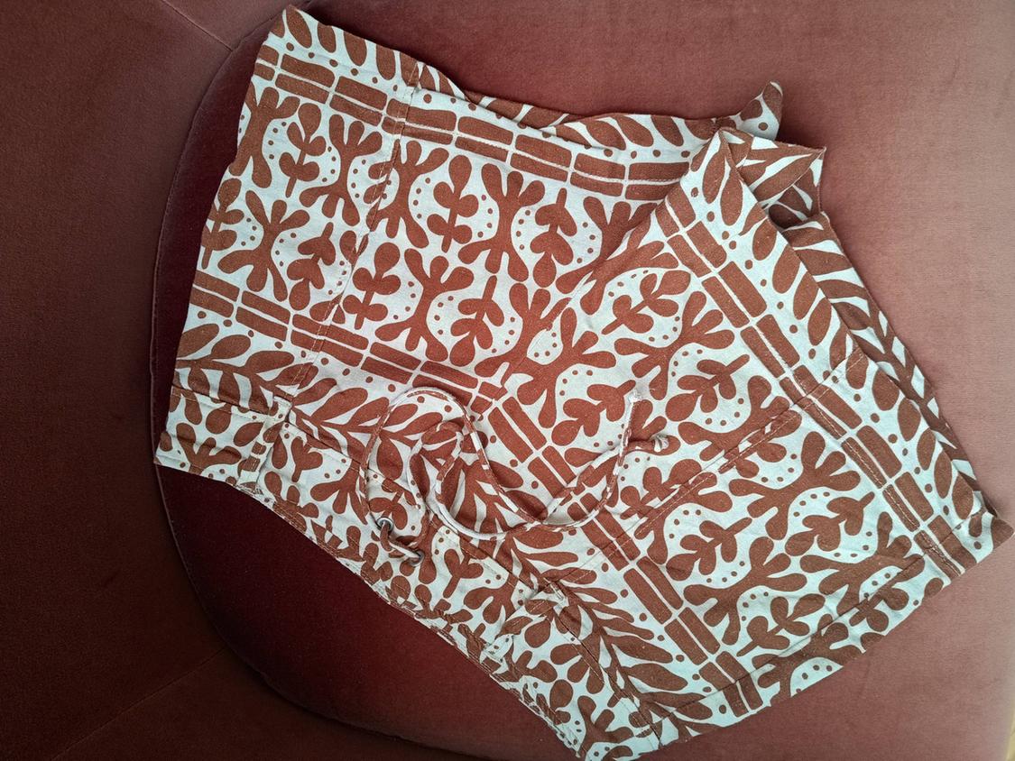 Folded shorts with a brown and white print and a drawstring waist, on a pink velvet surface.
