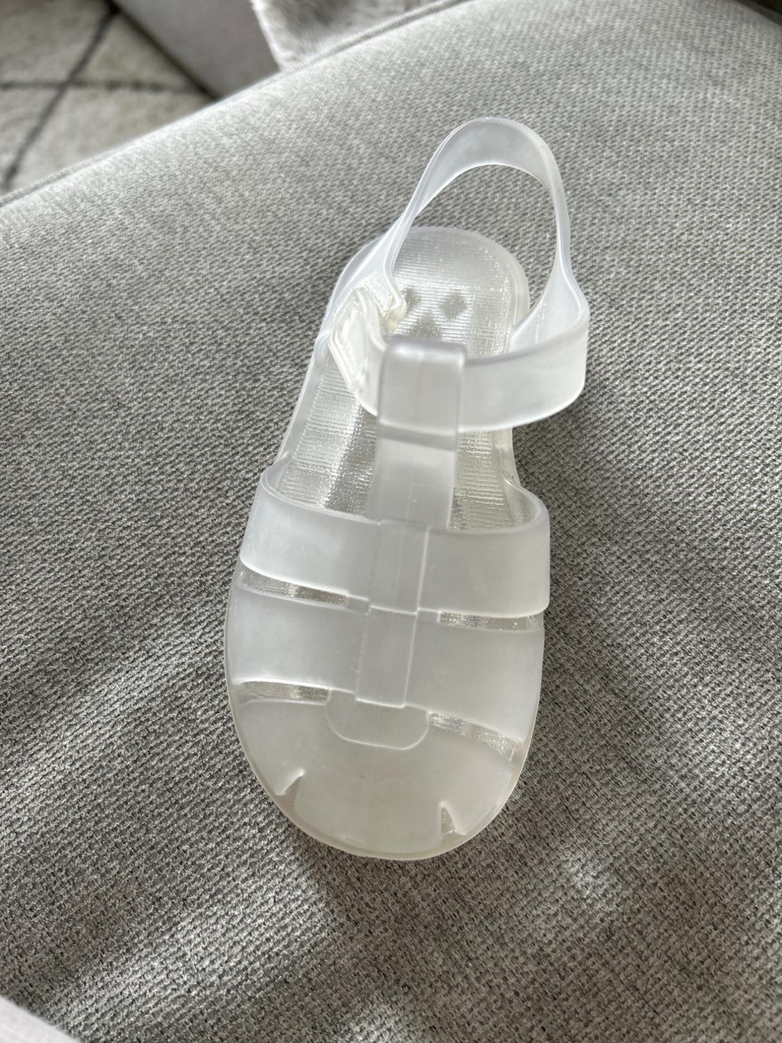 Transparent plastic sandal on a grey fabric background, top view, showcasing its simple and modern design.