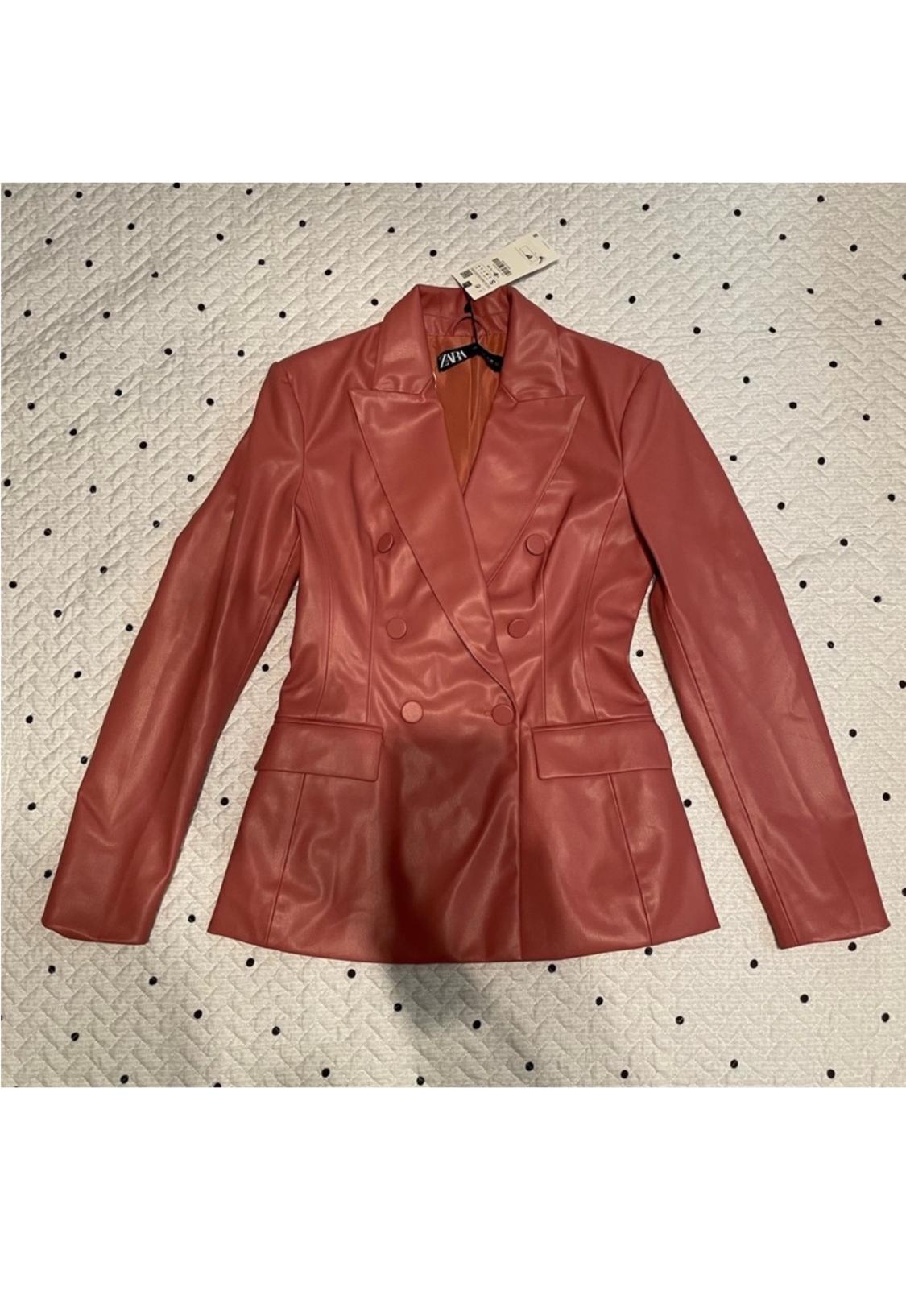 Double-breasted terracotta jacket on a white background with black dots. Visible label on the neck with the brand.