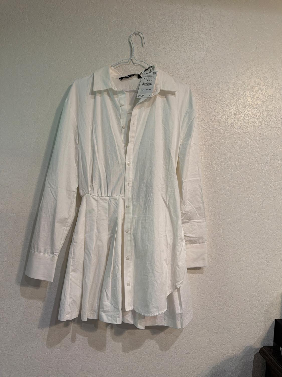 White long-sleeved shirt hanging on a hanger against a light-coloured wall. Visible tag with Japanese text and price.