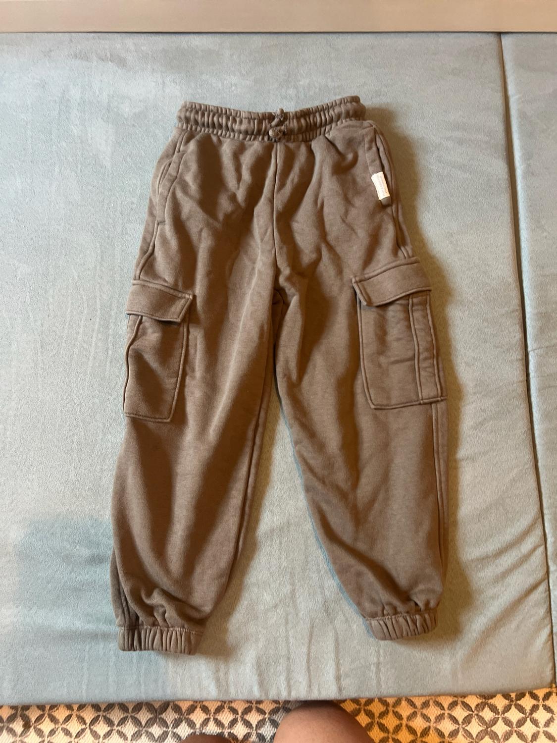 Brown cargo-style jogging bottoms with an elasticated waist, drawstring, side pockets and cuffed hems, on a blue surface.