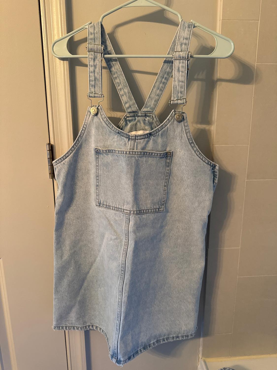 Light blue denim dress with crossover straps, hanging on a green hanger on a beige door.